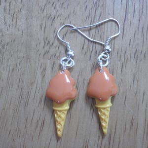 May include: A pair of dangle earrings featuring a brown and yellow ice cream cone design.