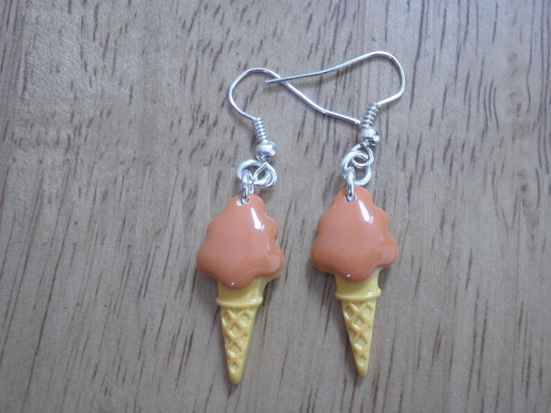 May include: A pair of dangle earrings featuring a brown and yellow ice cream cone design.