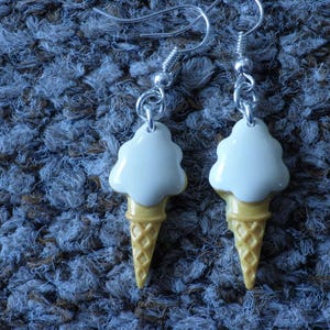 May include: A pair of white and yellow ice cream cone earrings. The ice cream is white and the cone is yellow with a waffle pattern.