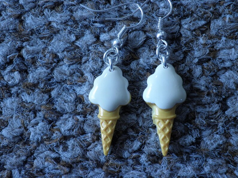 May include: A pair of white and yellow ice cream cone earrings. The ice cream is white and the cone is yellow with a waffle pattern.