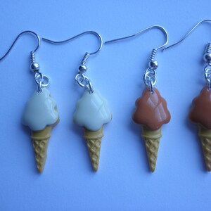 May include: Three pairs of dangle earrings featuring ice cream cone charms. One pair has white ice cream, one pair has brown ice cream, and one pair has a light brown ice cream.