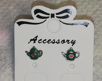 May include: A pair of green teapot earrings with red hearts on a white card with the word "Accessory" printed on it.