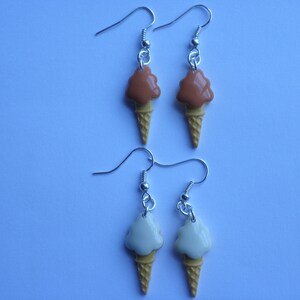 May include: A pair of silver earrings with ice cream cone charms. One pair features a brown and white ice cream cone charm, and the other pair features a white and yellow ice cream cone charm.