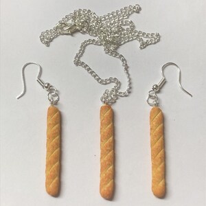 May include: A set of baguette-shaped earrings and a necklace. The jewellery is made of silver chain and polymer clay. The baguette charms are a light brown colour.