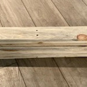 May include: A wooden shelf made of multiple planks of wood, painted white with a natural wood grain showing through. The shelf is made of several layers of wood, stacked on top of each other.