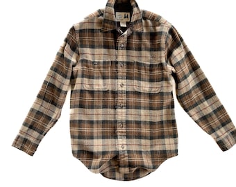 May include: A brown, tan, and black plaid flannel shirt with long sleeves. The shirt has two chest pockets and a button-down front. The collar is lined with a darker fabric. The shirt is made of a soft, woven material.