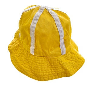 May include: A yellow bucket hat with white trim. The hat has a wide brim and a flat crown.