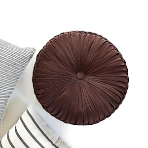 May include: A round brown pillow with a button in the center and a pleated design.