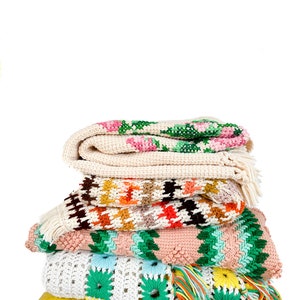 May include: A stack of crocheted blankets in various colors and patterns, including pink, green, white, and brown, are displayed on a yellow chair.