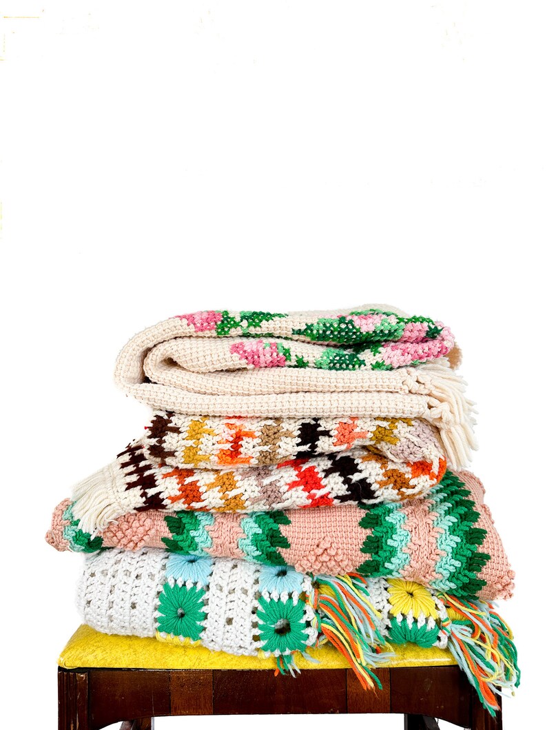 May include: A stack of crocheted blankets in various colors and patterns, including pink, green, white, and brown, are displayed on a yellow chair.
