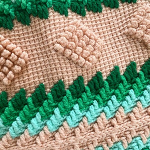 May include: Close-up of a crocheted blanket with a textured pattern. The blanket is made with pink, green, and blue yarn. The texture is created by using different stitches and techniques.