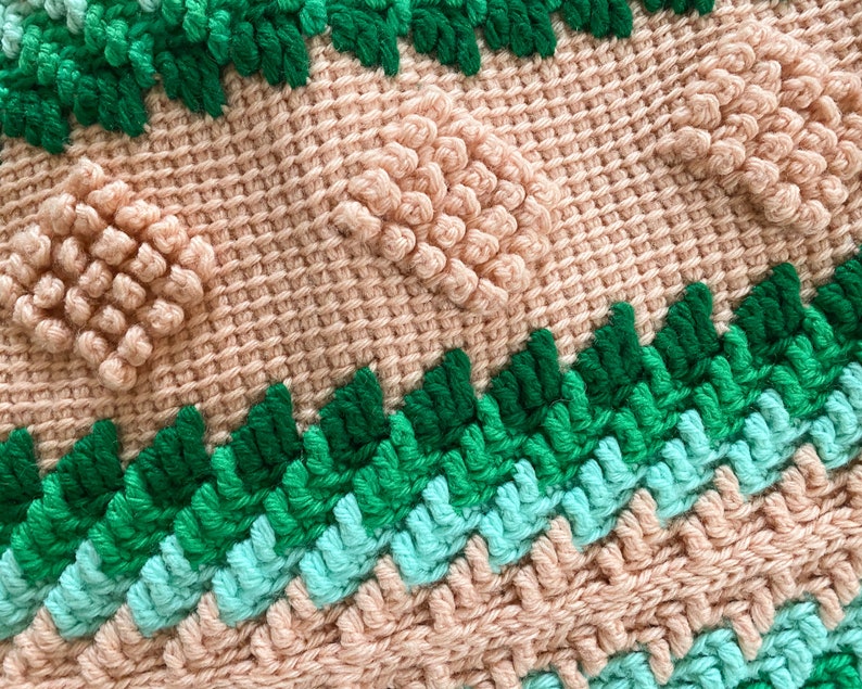 May include: Close-up of a crocheted blanket with a textured pattern. The blanket is made with pink, green, and blue yarn. The texture is created by using different stitches and techniques.