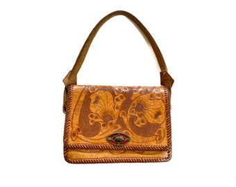 May include: A brown leather handbag with a floral design. The bag features a top handle and a clasp closure. The floral pattern is embossed on the front of the bag. The bag is approximately 8 inches wide and 6 inches tall.