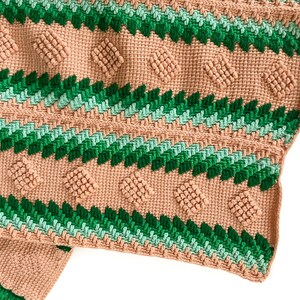 May include: A crocheted blanket with a geometric pattern in shades of green and pink.
