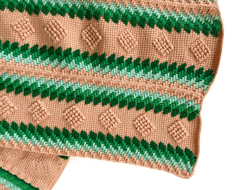 May include: A crocheted blanket with a geometric pattern in shades of green and pink.
