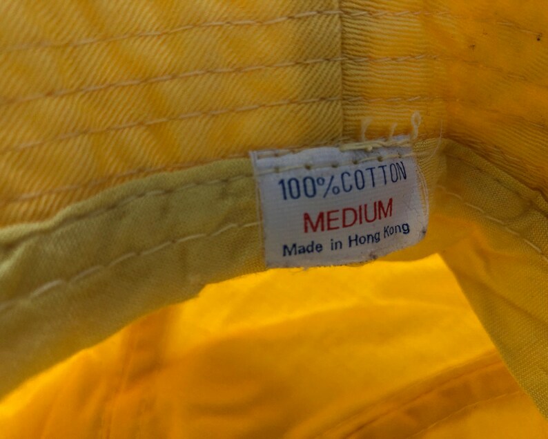May include: A yellow cotton bucket hat with a white label that reads "100% Cotton, Medium, Made in Hong Kong."