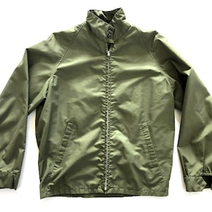 May include: A green zip-up jacket with a stand-up collar and a zipper closure. The jacket has two pockets on the front and elastic cuffs.