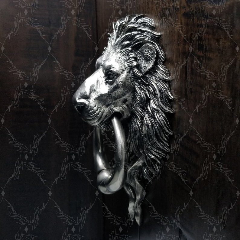 May include: A silver lion's head door knocker with a ring. The knocker is mounted on a wooden door.