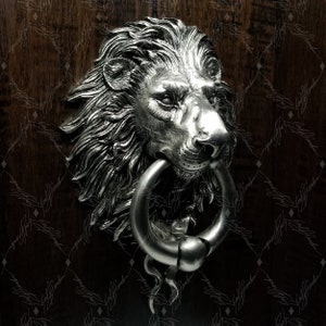 May include: A silver lion's head door knocker with a ring handle. The lion's head is detailed with a mane and a realistic expression.