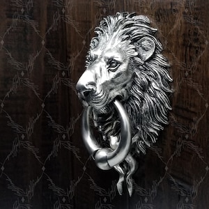 May include: Silver lion head door knocker with a ring. The lion's mane is detailed and the knocker has a realistic look.