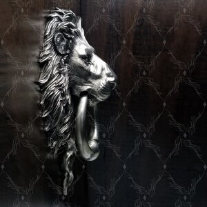May include: A silver lion's head door knocker with a ring handle. The knocker is mounted on a dark wooden door.