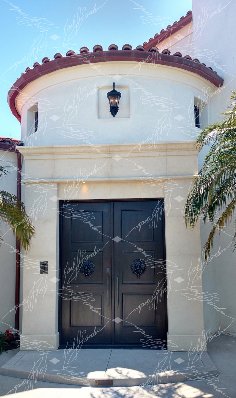 Pode incluir: Vista exterior de um edif&iacute;cio com uma entrada de porta dupla castanha escura. A porta tem aldravas com cabe&ccedil;a de le&atilde;o. Acima da porta, h&aacute; uma fachada de pedra de cor clara. O telhado tem telhas vermelhas. Uma lanterna preta est&aacute; pendurada acima da porta.