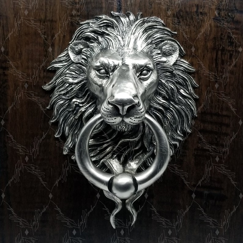 May include: A silver lion's head door knocker with a ring. The lion's head is detailed with a mane and a fierce expression.