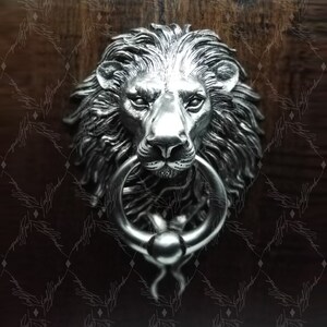May include: A silver lion's head door knocker with a ring. The lion's head is detailed with a mane and a realistic expression.