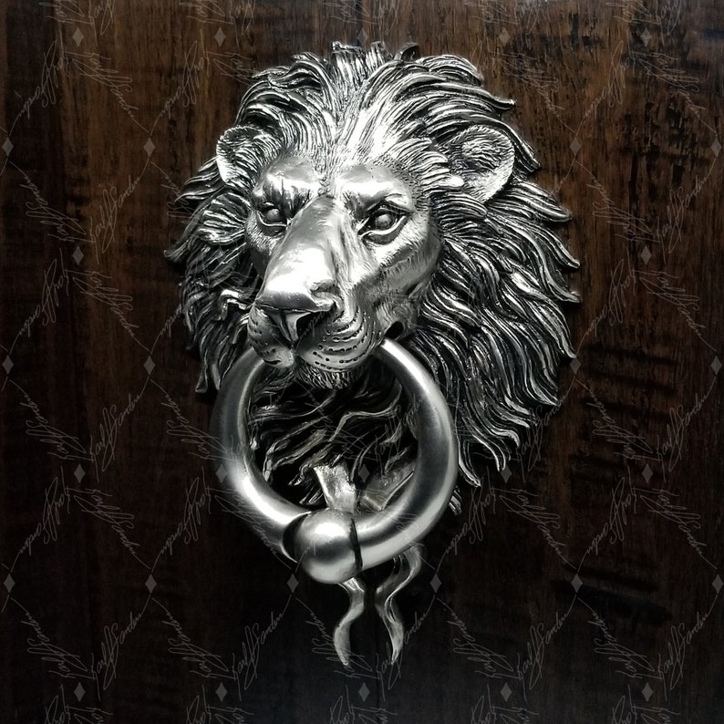 May include: A silver lion's head door knocker with a round ring. The knocker is mounted on a wooden door.