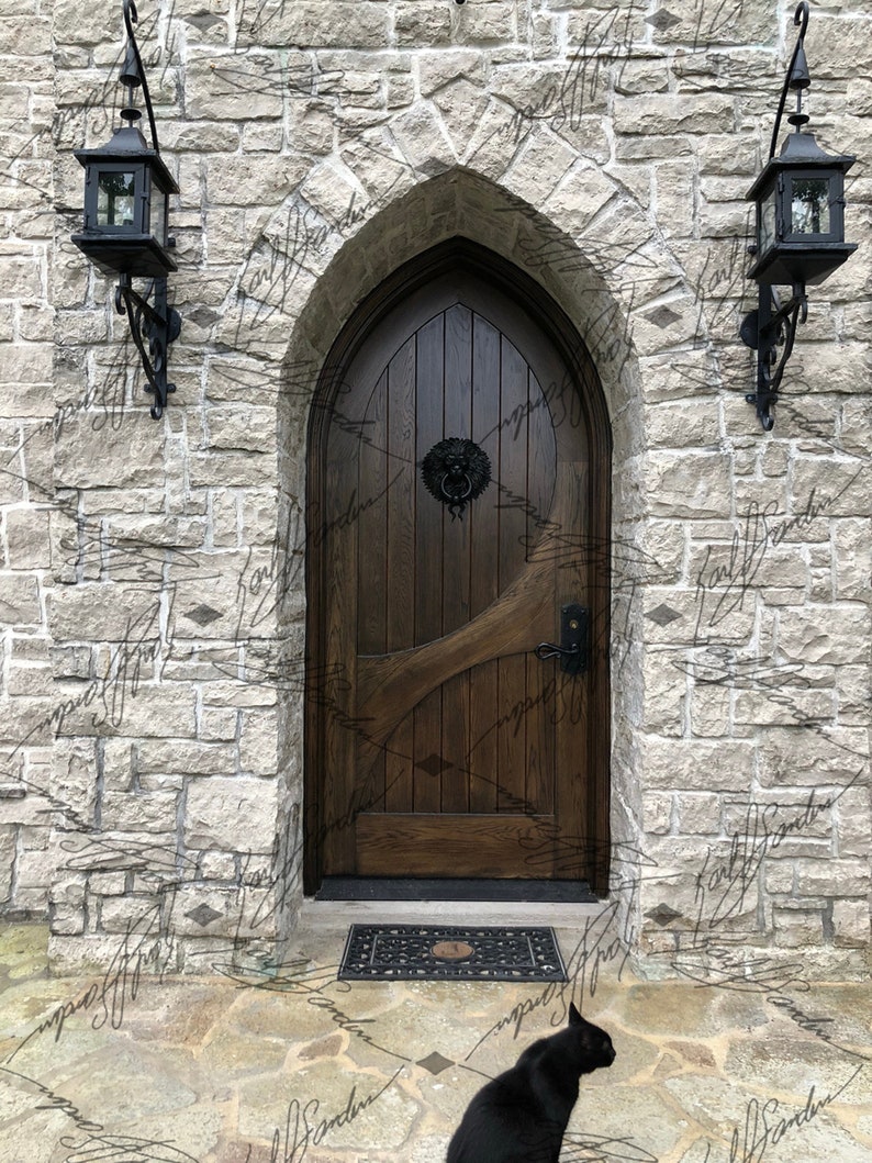 Pode incluir: Uma porta arqueada de madeira escura com uma aldrava em forma de cabe&ccedil;a de le&atilde;o est&aacute; situada numa parede de pedra. Duas lanternas pretas penduram-se em ambos os lados da porta. Um gato preto est&aacute; sentado no p&aacute;tio de pedra em frente &agrave; porta.