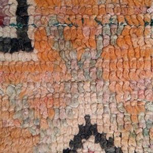 May include: Close-up of a woven rug with a geometric pattern in shades of pink, orange, and black.