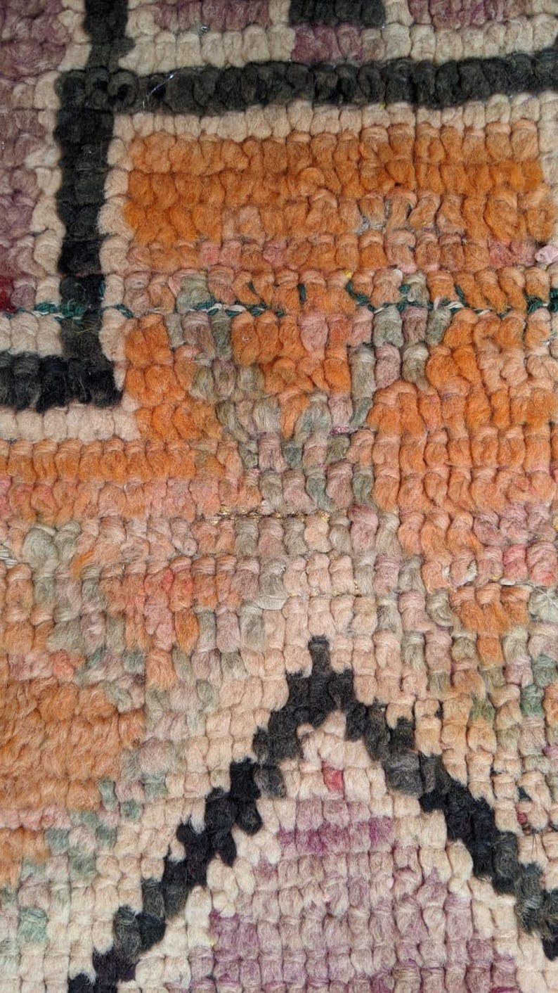 May include: Close-up of a woven rug with a geometric pattern in shades of pink, orange, and black.