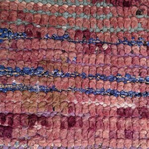 May include: Close-up of a woven rug with a pink, blue, and white pattern. The rug is made of thick, textured yarn and has a slightly distressed look.