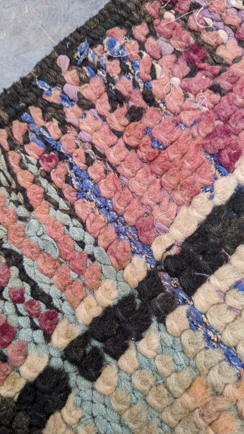 May include: Close-up of a colorful woven rug with a variety of colors including pink, blue, black, and white. The rug is made of thick, fuzzy yarn and has a textured surface.