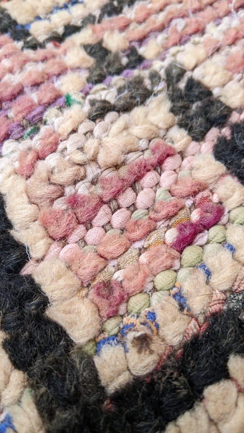 May include: Close-up of a colorful woven rug with pink, beige, and black yarn. The rug has a textured, hand-woven look.