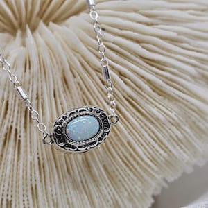 May include: A silver chain necklace with a white opal stone set in a silver filigree pendant.