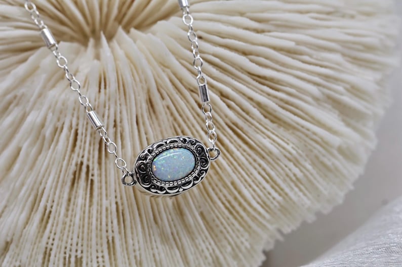May include: A silver chain necklace with a white opal stone set in a silver filigree pendant.