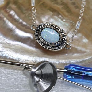 May include: A silver chain necklace with a white opal gemstone set in a silver filigree pendant. The pendant is oval shaped and has a detailed design.