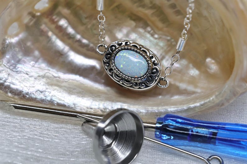 May include: A silver chain necklace with a white opal gemstone set in a silver filigree pendant. The pendant is oval shaped and has a detailed design.