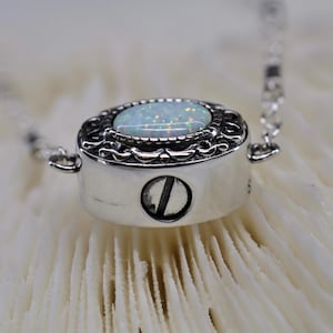 May include: A silver necklace with a white opal stone set in a detailed filigree design. The pendant has a screw closure.