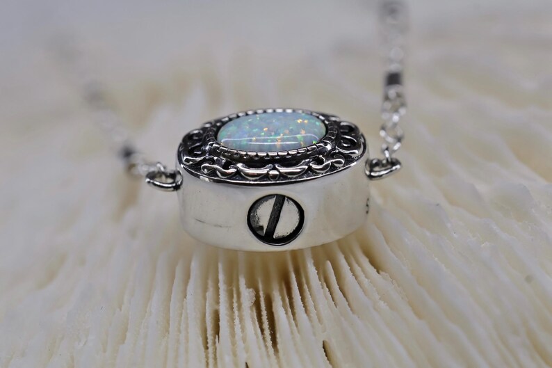 May include: A silver necklace with a white opal stone set in a detailed filigree design. The pendant has a screw closure.