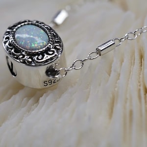 May include: A silver chain necklace with a pendant featuring a white opal stone set in a silver ornate frame. The pendant is marked with "S925" on the side.