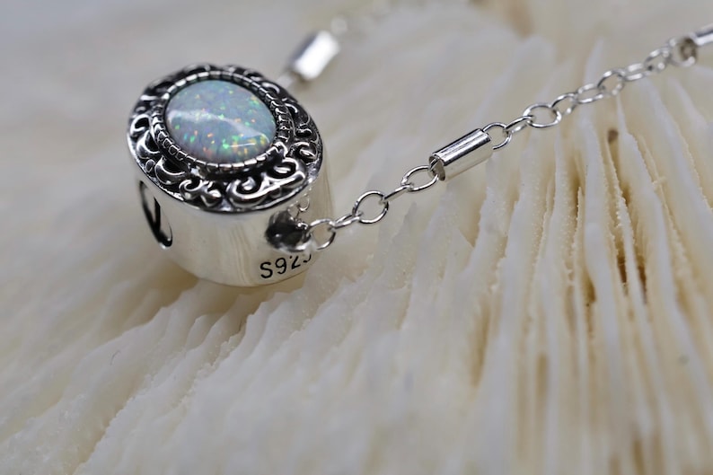 May include: A silver chain necklace with a pendant featuring a white opal stone set in a silver ornate frame. The pendant is marked with "S925" on the side.