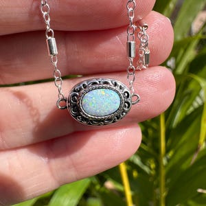 May include: A silver chain necklace with a white opal gemstone set in a silver filigree pendant.