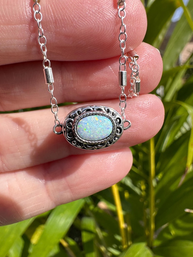 May include: A silver chain necklace with a white opal gemstone set in a silver filigree pendant.