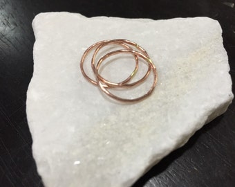 May include: Three thin gold rings stacked on top of each other on a white marble surface.