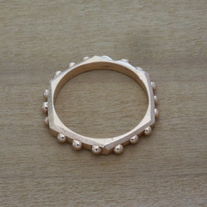May include: A gold-toned ring with a hexagonal shape and a beaded edge.