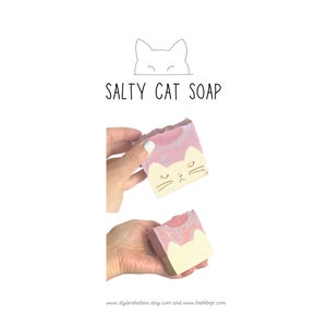 May include: A pink and white soap bar with a cat face design. The soap is labeled "Salty Cat Soap".