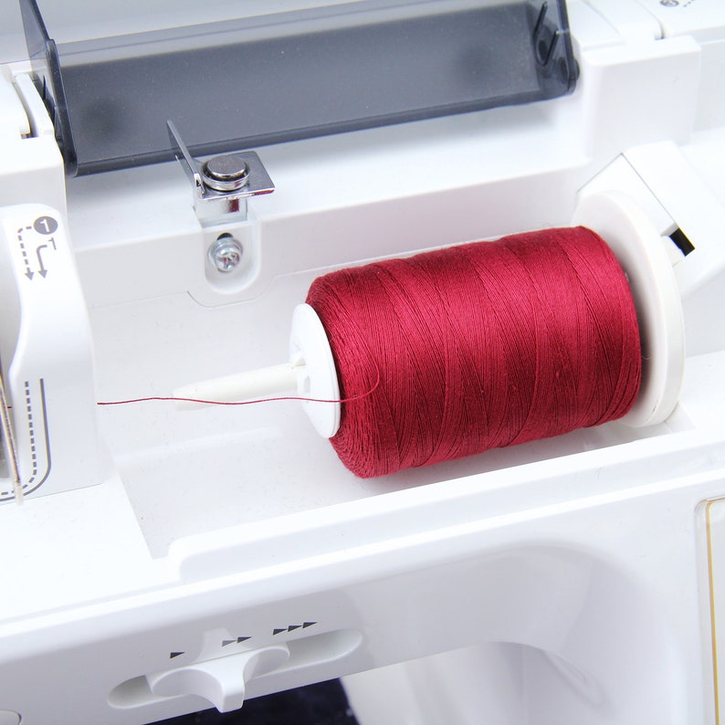 Pode incluir: Um close-up de uma m&aacute;quina de costura branca com um carretel de fio vermelho no enrola-bobina.