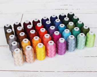 May include: A collection of 36 spools of embroidery thread in various colors, arranged in a triangular shape on a white wooden surface.